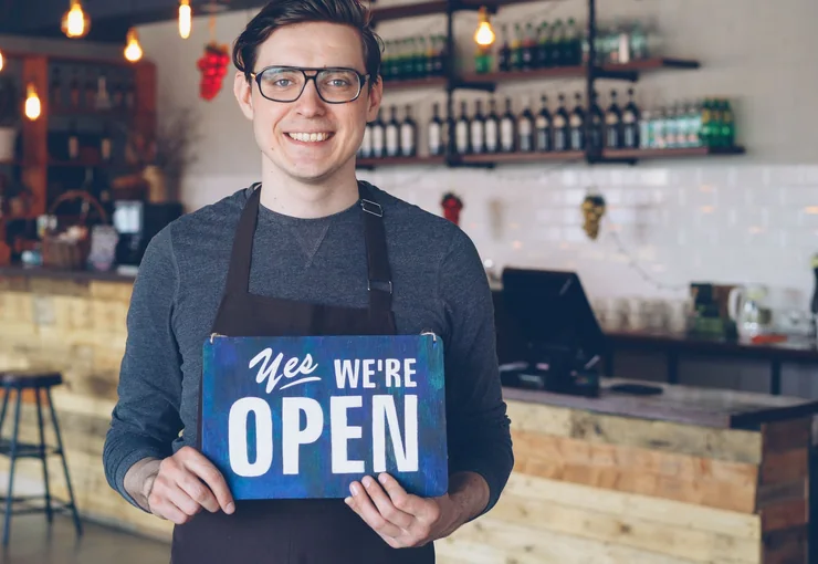 A small business owner holding an open sign in his shop