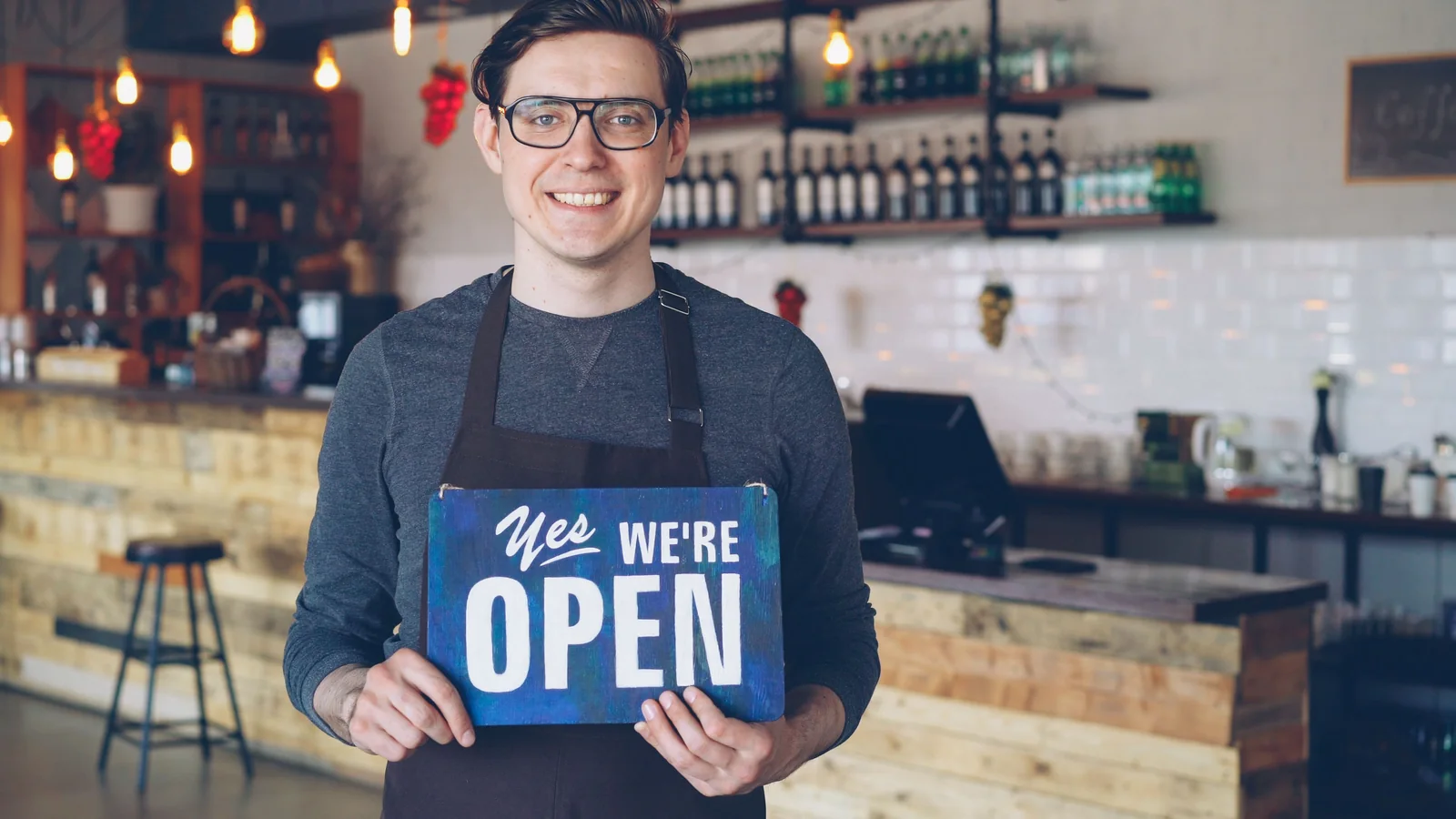 A small business owner standing in his shop holding a hand-painted open sign